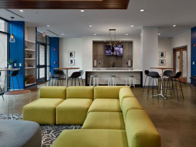 Spacious community clubhouse lounge with a social kitchen counter, white barstools, and vibrant seating areas at Madison@McLean Midtown apartments in Memphis.