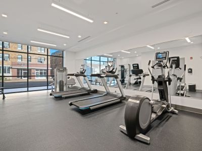 State-of-the-art fitness center equipped with commercial treadmills and ellipticals facing a large wall mirror at Madison@McLean Midtown apartments in Memphis.