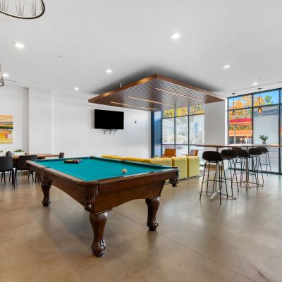 Community game room area featuring a classic wooden pool table, high-top bar seating, and large windows at Madison@McLean Midtown apartments in Memphis.