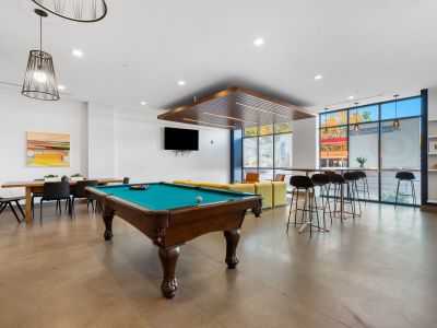 Community game room area featuring a classic wooden pool table, high-top bar seating, and large windows at Madison@McLean Midtown apartments in Memphis.
