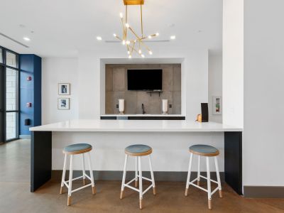 Clubhouse kitchen island bar with white countertops, three modern stools, and a geometric gold chandelier at Madison@McLean Midtown apartments in Memphis.