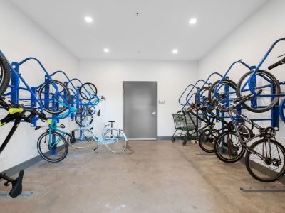 Secure indoor resident bicycle storage room equipped with blue heavy-duty wall-mounted vertical racks at Madison@McLean Midtown apartments in Memphis.