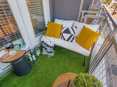 Cozy private apartment balcony styled with artificial turf flooring, a white bench loveseat, and accent pillows at Madison@McLean Midtown apartments in Memphis.
