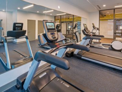 Commercial gym and fitness center layout featuring treadmills, an elliptical machine, and floor-to-ceiling mirrors at Madison@McLean Midtown apartments in Memphis.