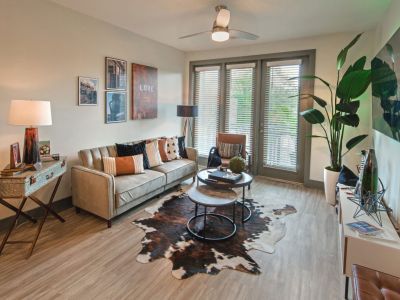 Fully furnished apartment living room featuring a cowhide rug, neutral sofa, and glass balcony entry doors at Madison@McLean Midtown apartments in Memphis.