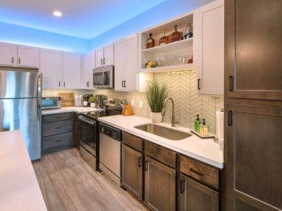 Contemporary apartment kitchen showing white upper cabinets, dark lower cabinets, stainless steel appliances, and a chevron tile backsplash at Madison@McLean Midtown apartments in Memphis.