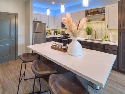 Modern kitchen featuring a spacious white quartz island with breakfast bar stools, stainless steel appliances, and ambient blue under-cabinet lighting at Madison@McLean Midtown apartments in Memphis.