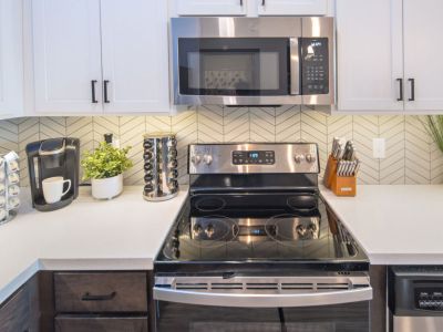 Upgraded kitchen countertop space showcasing a stainless steel smooth-top electric range, matching microwave, and a chevron patterned tile backsplash at Madison@McLean Midtown apartments in Memphis.