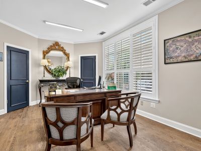 Leasing office interior featuring a classic wooden executive desk, decorative armchairs, white plantation shutters, navy blue doors, and a framed map layout of the property on the wall at The Magnolias apartments in Hernando, MS.