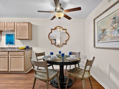 Dedicated apartment dining area showcasing a round dark wood table set for four, wooden chairs, an overhead ceiling fan, and a decorative gold-framed accent mirror on the wall at The Magnolias apartments in Hernando, MS.
