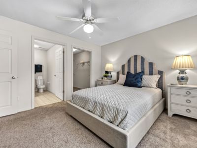Spacious bedroom highlighting the upholstered bed frame, light walls, and open doorways leading to an en-suite bathroom and walk-in closet at The Magnolias apartments in Hernando, MS.