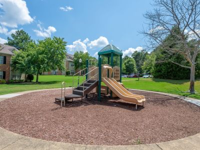On-site children's playground structure with slides and climbing stairs over a wood chip surface at The Magnolias apartments in Hernando, MS.