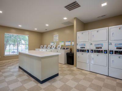 On-site laundry facility equipped with a central folding island table, commercial washing machines, and stacked white dryers at The Magnolias apartments in Hernando, MS