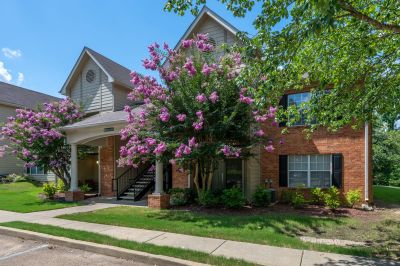 Two-story brick residential building entrance accented by vibrant purple blooming crape myrtle trees and a concrete sidewalk at The Magnolias apartments in Hernando, MS.