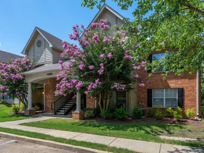 Two-story brick residential building entrance accented by vibrant purple blooming crape myrtle trees and a concrete sidewalk at The Magnolias apartments in Hernando, MS.