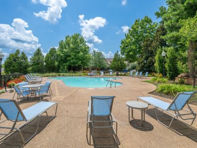 Resort-style community swimming pool with lounge chairs, a patio table set, and surrounding green trees under a blue sky at The Magnolias apartments in Hernando, MS.