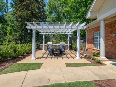 Outdoor community picnic space under a white wooden pergola with grilling stations and a large dining table at The Magnolias apartments in Hernando, MS