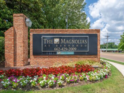 Brick monument property entrance sign adorned with colorful seasonal flower beds at The Magnolias apartments in Hernando, MS.