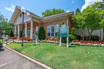 Information center entrance with a directional sign post, manicured lawns, and red and white flowers at The Magnolias apartments in Hernando, MS.