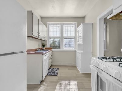 Historic galley kitchen featuring white cabinetry, a gas range stove, white refrigerator, and dining hutch within a St. Regis style home at Midtown Place apartments in Memphis.