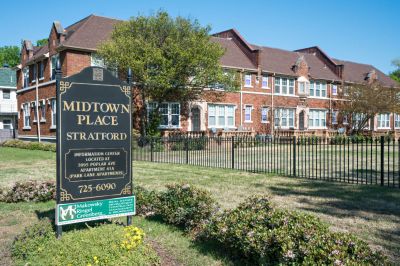 Historic multi-story red brick residential buildings behind a black metal fence with a community sign for Stratford Place at Midtown Place apartments in Memphis.