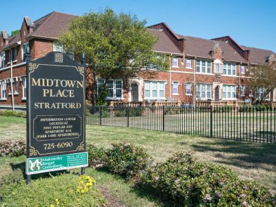 Historic multi-story red brick residential buildings behind a black metal fence with a community sign for Stratford Place at Midtown Place apartments in Memphis.