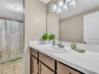 Updated apartment bathroom featuring a long white vanity countertop, dark wood cabinets, a large mirror, and a leaf-patterned shower curtain at Stratford Place in Memphis.