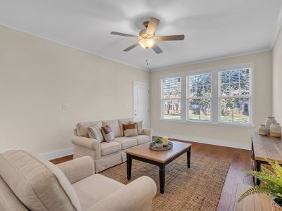 Bright renovated living room layout highlighting rich hardwood flooring, neutral walls, a ceiling fan, and large windows at Stratford Place in Memphis.