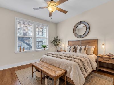 Spacious renovated apartment bedroom featuring warm wood floors, matching wooden furniture, and a ceiling fan at Stratford Place in Memphis.