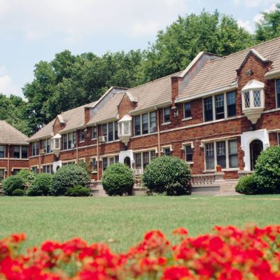 Scenic view across a manicured green lawn and vibrant red flowers toward the historic Tudor-style brick residential buildings at Stratford Place apartments in Memphis.