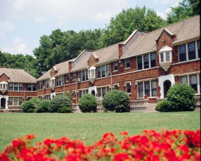 Scenic view across a manicured green lawn and vibrant red flowers toward the historic Tudor-style brick residential buildings at Stratford Place apartments in Memphis.