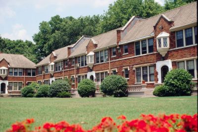 Scenic view across a manicured green lawn and vibrant red flowers toward the historic Tudor-style brick residential buildings at Stratford Place apartments in Memphis.