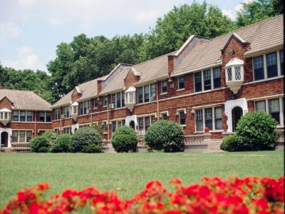 Scenic view across a manicured green lawn and vibrant red flowers toward the historic Tudor-style brick residential buildings at Stratford Place apartments in Memphis.