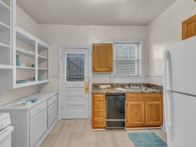 Historic apartment kitchen showcasing natural wood lower cabinetry, a dishwasher, white open pantry shelving, and a glass-paneled back door at Midtown Place The Tuscany in Memphis.
