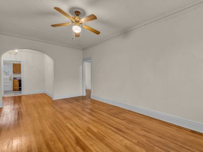 Spacious living room featuring glossy hardwood flooring, neutral walls, a ceiling fan, and distinctive architectural arches at Midtown Place The Tuscany in Memphis.
