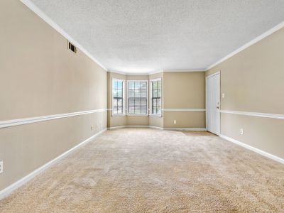 Empty living room layout showcasing a deep bay window with built-in blinds, neutral tan walls, and plush beige carpeting at Monticello apartments in Memphis