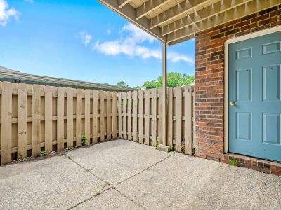 Fenced concrete patio area outside a ground-level brick residential unit with a blue utility door at Monticello apartments in Memphis.