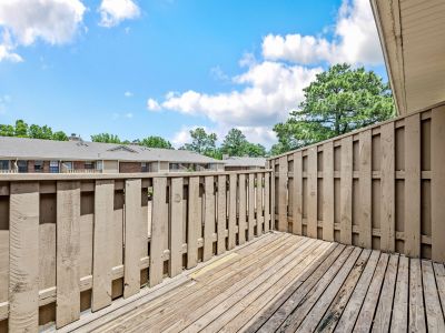 Private wooden balcony deck enclosed by a high privacy railing under a bright sky at Monticello apartments in Memphis.