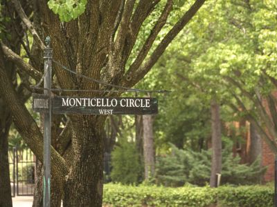 Vintage-style dark green street sign reading Monticello Circle West surrounded by mature shade trees at Monticello apartments in Memphis.