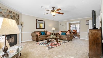 Spacious living room featuring tan carpet, a ceiling fan, comfortable brown sofas, and a traditional fireplace at Monticello apartments in Memphis.