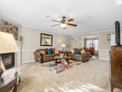 Spacious living room featuring tan carpet, a ceiling fan, comfortable brown sofas, and a traditional fireplace at Monticello apartments in Memphis.