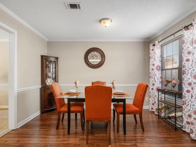 Formal dining area showing a glass-top table paired with modern orange upholstered chairs on wood-style floors at Monticello apartments in Memphis.