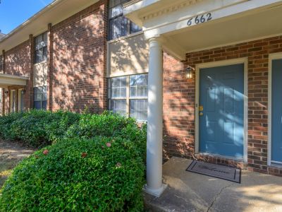 Apartment building entrance featuring a white column porch structure, a blue entry door, and manicured green hedges at Monticello apartments in Memphis.