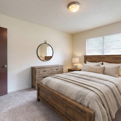 Cozy primary bedroom featuring a rustic wooden bed frame, matching nightstands, neutral bedding, and a closet with bifold doors at Pinewood Manor apartments and townhomes in Memphis.