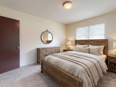 Cozy primary bedroom featuring a rustic wooden bed frame, matching nightstands, neutral bedding, and a closet with bifold doors at Pinewood Manor apartments and townhomes in Memphis.