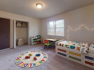 Decorated kids bedroom featuring a daybed with colorful storage drawers, string lights on the wall, an alphabet rug, and a small play table at Pinewood Manor apartments and townhomes in Memphis.