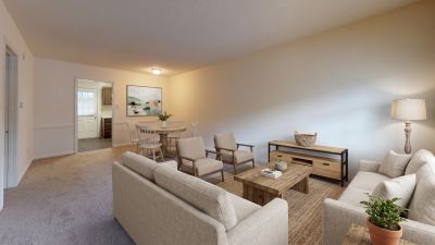 living room layout with neutral couches, light wood tables, a woven rug, and a separate dining area at Pinewood Manor apartments and townhomes in Memphis.
