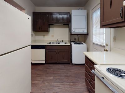Classic apartment kitchen featuring dark wood cabinets, white appliances, and an in-unit stacked washer and dryer at Pinewood Manor apartments and townhomes in Memphis.