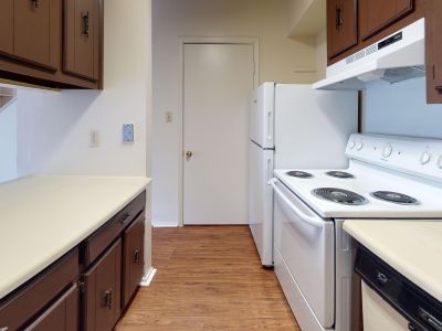 Classic apartment kitchen featuring dark wood cabinets, white appliances, and an in-unit stacked washer and dryer at Pinewood Manor apartments and townhomes in Memphis.