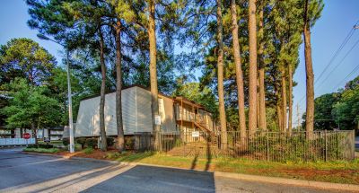 Gated residential building exterior tucked behind a grove of tall pine trees at Pinewood Manor apartments and townhomes in Memphis.